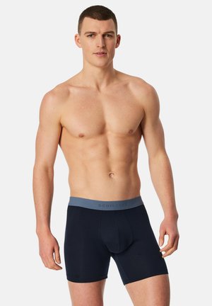 Dunkelblaue Boxer-Shorts mit einem hellgrauen Bund, der den Markennamen "Schiesser" trägt. Hergestellt aus einem glatten, dehnbaren Stoff, eng anliegender Schnitt.