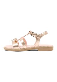 Metaliczny złoty sandał z trzema poziomymi paskami, regulowaną klamrą przy kostce i płaską gumową podeszwą. Różowa wkładka. Gładka faktura.