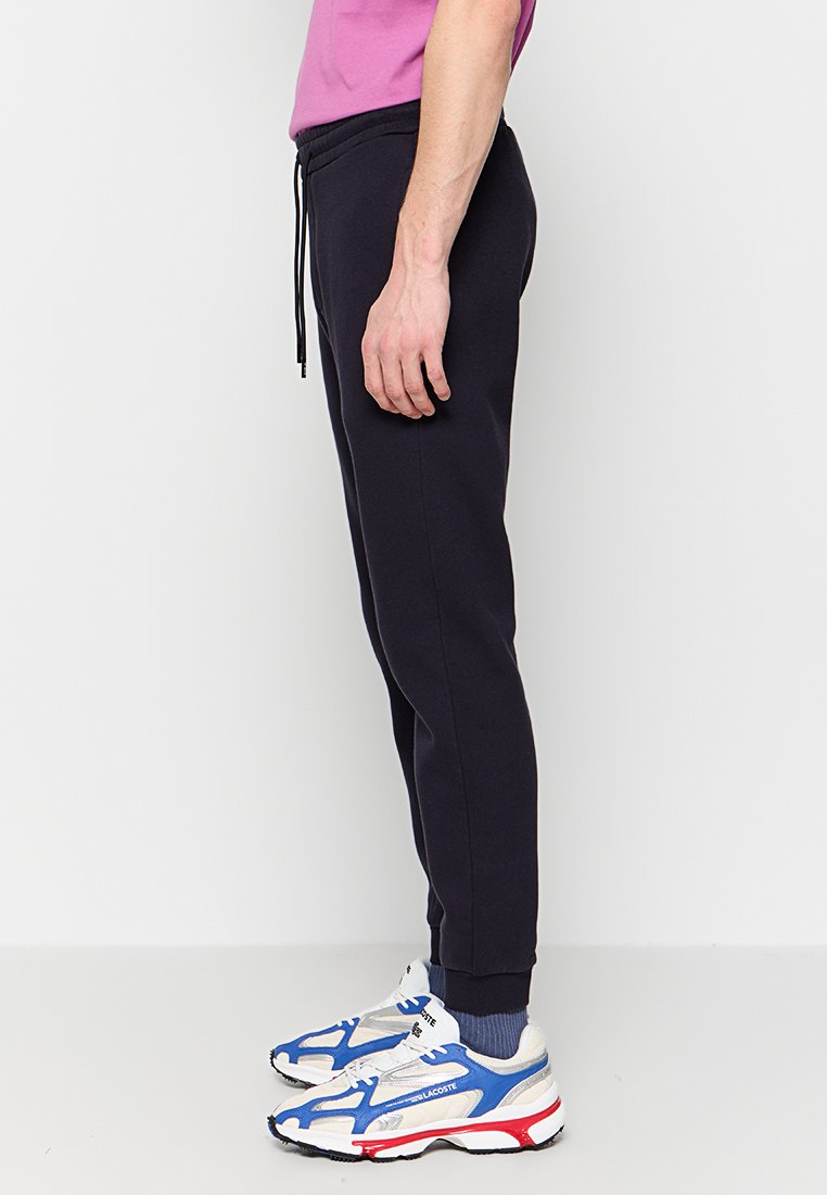 Pantaloni della tuta blu scuro con elastico in vita e stringa, gamba affusolata, texture morbida. Abbinati a sneakers sportive bianche e blu.