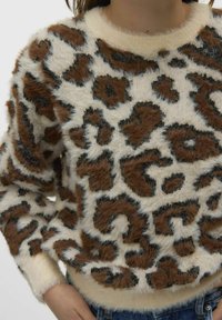 Weicher, flauschiger Pullover mit braunem und schwarzem Leopardenmuster, getragen mit blauen Jeans, mit gerippten Bündchen und rundem Ausschnitt.