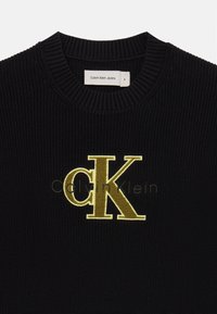 Črn rebrast pulover s krožnim ovratnikom. Ima vezenje z zlatim CK logotipom in oznako "Calvin Klein Jeans" na ovratniku. Teksturirana tkanina.
