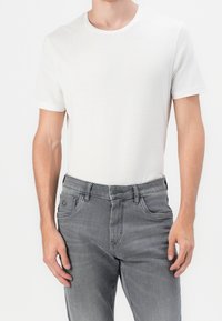 Biała bawełniana koszulka z krótkim rękawem, noszona z szarymi dżinsami z denimu o klasycznym kroju, z przeszyciami i przednimi kieszeniami.