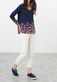 Marinblå V-ringad långärmad topp med blommönster vid fållen, matchad med vita cropped byxor och marinblå snörskor.