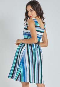 Vestido a rayas con un cuerpo ajustado y falda acampanada. Los colores incluyen azul, negro y verde. Está confeccionado en una tela liviana con un acabado texturizado.