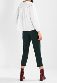 Blusa bianca con punti in rilievo e schiena a oblò, abbinata a pantaloni cropped verdi. Indossata con stivaletti con tacco bordeaux.