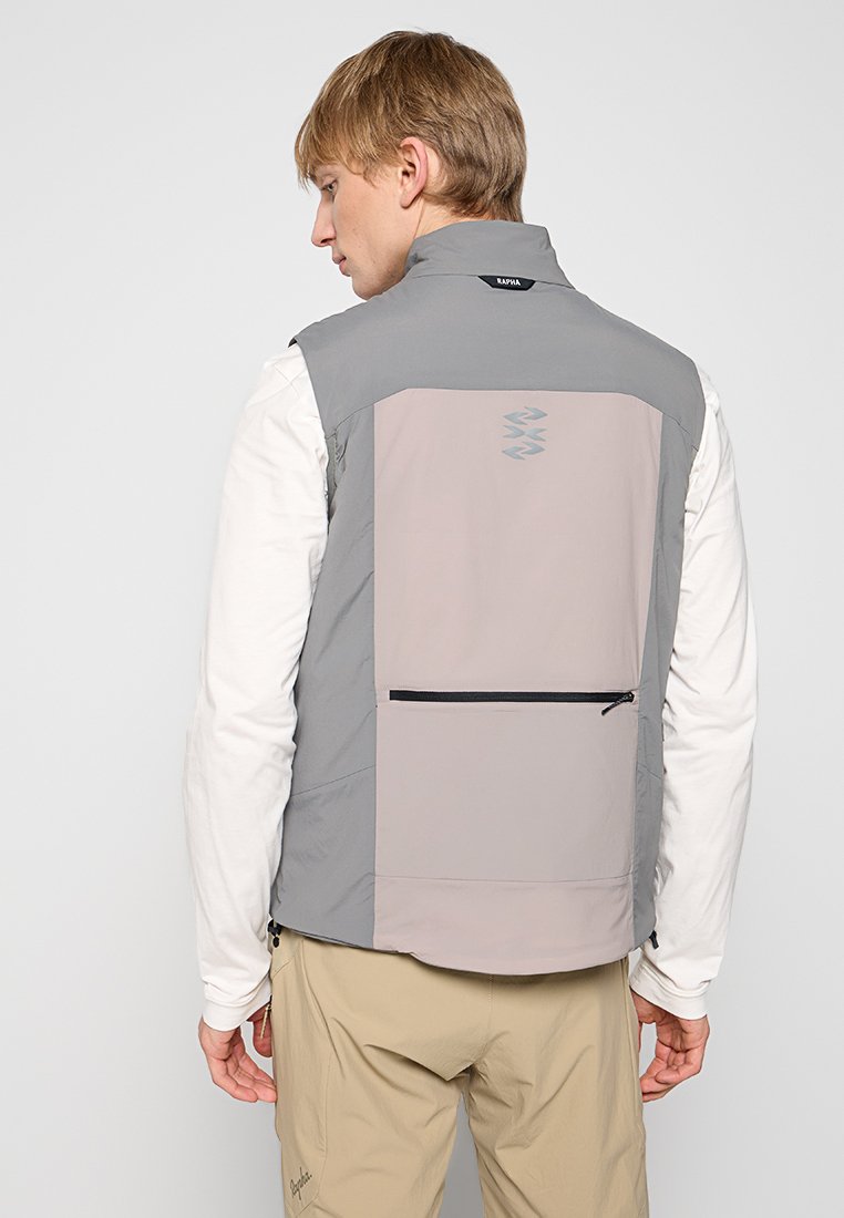 Grau und hellbeige Weste mit hohem Kragen, Rückentasche, Reißverschluss und Logodetail. Getragen über einem langärmeligen Hemd.