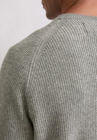 Pull en tricot gris avec un motif texturé, doté d'un col rond et d'une coupe raglan. Le tissu semble doux et extensible.