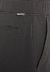Mörkgrå, lätta joggers i tyg med en slät yta, som har en sidficka och en liten "icebreaker"-etikett. Diskret sömnadsdetalj.
