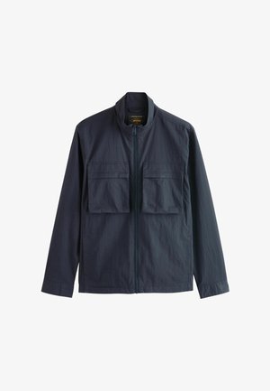Donkerblauwe lichtgewicht jas met frontrits en twee grote borstzakken met kleppen, weergegeven op een witte achtergrond.
