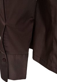 Κοντινό πλάνο σκούρου καφέ μανικιού και μανσετών πουκάμισου με ένα μόνο σκούρο κουμπί, που δείχνει την υφή του υφάσματος και τις λεπτομέρειες της ραφής.
