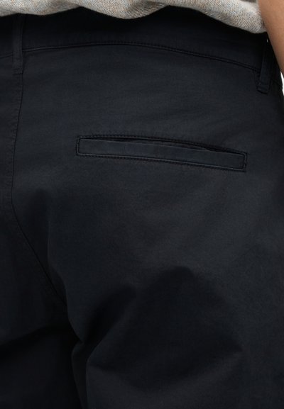 Pantalon bleu marine foncé en tissu doux, avec une poche arrière à rabat simple et des coutures nettes. Look minimaliste et ajusté.