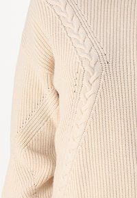 Maglione lavorato a maglia in beige chiaro con un motivo a treccia texturizzato lungo la cucitura della spalla e dettagli a coste su corpo e maniche.