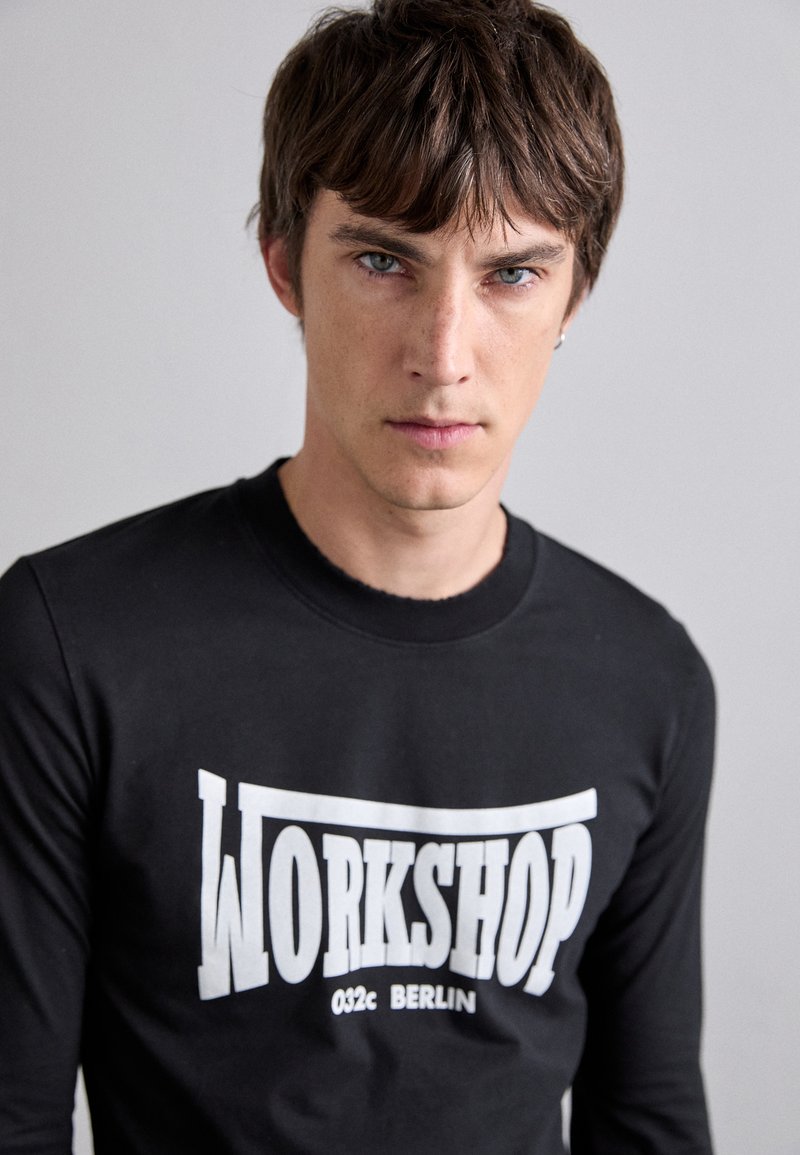 Schwarzes Langarmshirt mit großem weißen "WORKSHOP 032c BERLIN"-Schriftzug. Glattes Material mit Rundhalsausschnitt. Eng anliegende Passform.