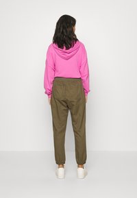 Pink hættetrøje med elastiske manchetter, parret med olivengrønne tapered bukser med elastisk talje og ankelmanchetter. Hvide sneakers.