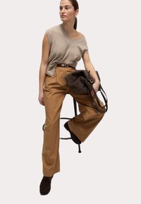 Beige stickad topp med sned halsringning, kombinerad med högmidjade bruna vida byxor. Mörkbrun handväska med rem. Bruna skor.