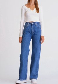 Top corto de manga larga blanco condo borde festoneado, combinado con jeans rectos de cintura alta en un tono azul claro y zapatillas blancas.