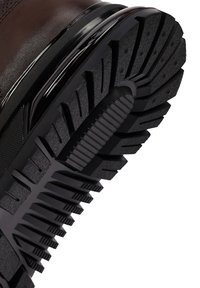 Bruine leren laars met een gestructureerde zwarte rubberen zool met diepe profielgroeven voor grip en een verhoogde zwarte accent rond de zool.