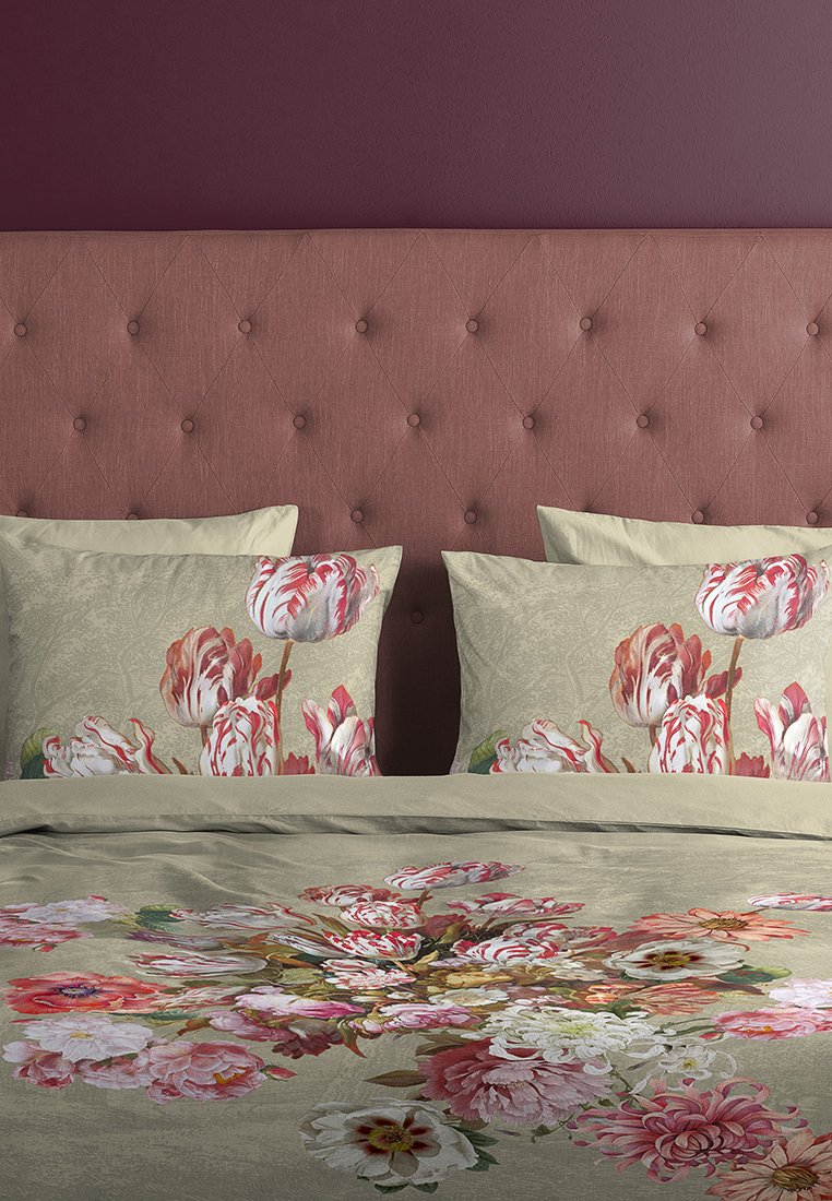 Ett tuftat huvudgavel i mauve-rosa bakom sängen med beige sängkläder och kuddar med röda och vita tulpanblommönster.