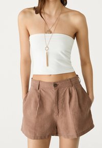 Top corto bianco senza spalline abbinato a pantaloni corti beige con pieghe, dotati di tasche laterali e chiusura con bottone, su uno sfondo neutro.