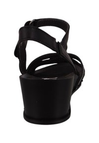 Sandalia negra con un tacón ancho, que presenta múltiples correas y una punta redondeada. La parte superior tiene una textura suave con detalles recortados.