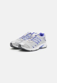 Adidași albi cu accente violet, având un superior din plasă, talpă căptușită și talpă exterioară din cauciuc texturat pentru aderență.
