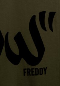 Tejido de color verde oliva oscuro con un gran texto gráfico negro en letras estilizadas y la palabra "FREDDY" posicionada debajo.