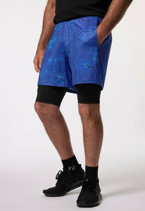 Blauwe sportshorts met een bliksemschichtpatroon, gemaakt van lichtgewicht materiaal, met zijzakken en gedragen over zwarte compressieshorts.
