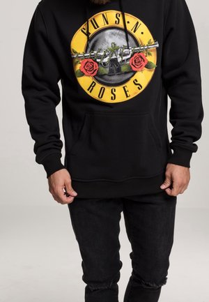 Homme portant un sweat à capuche noir avec le logo de Guns N' Roses représentant deux roses rouges et un pistolet entouré de fils barbelés.