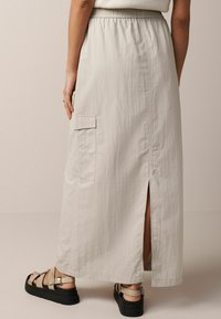 Jupe midi beige clair en tissu léger, avec une taille élastique, une poche cargo sur les côtés et une fente sur le côté pour plus de facilité de mouvement.