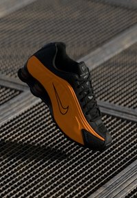 Black and orange Nike shoe featuring a textured upper, smooth accents, and a prominent Swoosh logo; designed with a cushioned sole.