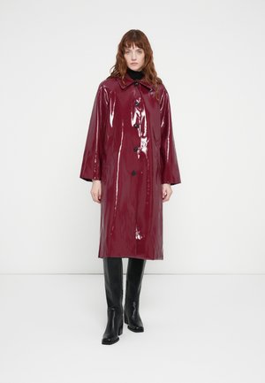 Burgundy glossy raincoat with a collar, button closure, and wide sleeves, paired with knee-high black boots. Smooth texture, long design.