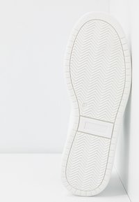 Semelle de basket blanche avec motif de bande de poisson, taille 37 marquée près de la voûte plantaire, présentée à la verticale sur un fond blanc.