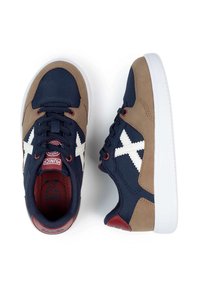 Zapatillas marinas y beige con costuras blancas y detalles rojos. Presentan una parte superior de tela y ante, cordones redondos y una suela de goma blanca.