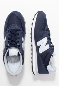 Marinblå sneakers i mesh och mocka. Utrustade med en vit 'N'-logotyp, ytterligare grå detaljer och en texturerad svart gummisula.