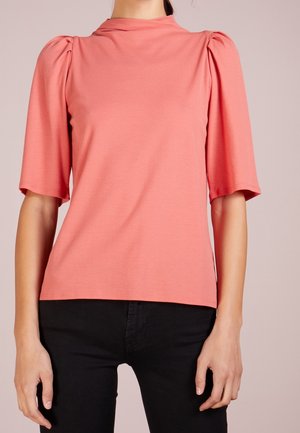 Haut corail à manches courtes bouffantes, texture douce, col montant, coupe décontractée, associé à un bas noir.