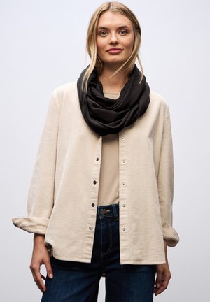 Beige textuurknopenhemd met lange mouwen, gedragen over een lichte top, gecombineerd met een zwarte infinity-sjaal en donkere jeans.