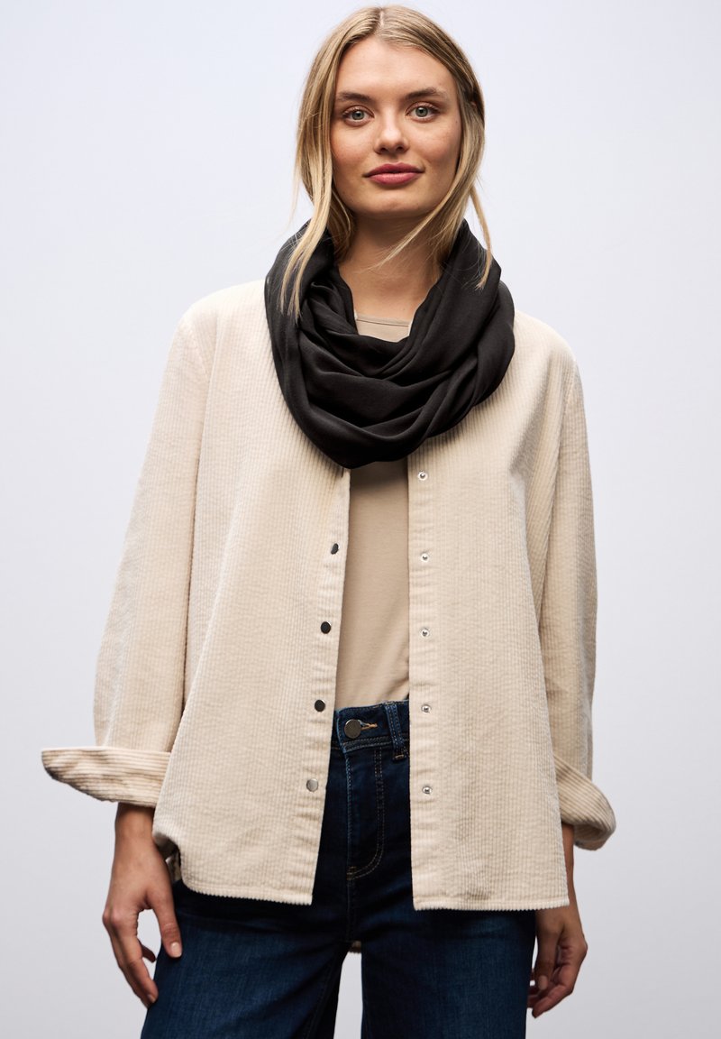 Beige tekstureret skjorte med lange ærmer, båret over en lyseblå top, parret med et sort infinity tørklæde og mørke jeans.