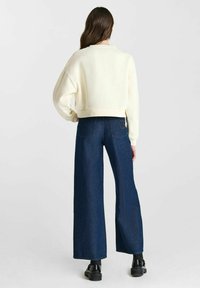 Witte cropped sweatshirt met brede mouwen, gecombineerd met hooggeplaatste, wijde donkerblauwe denim jeans. Zwarte chunky schoenen maken de outfit compleet.
