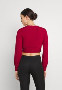 Top cropped vermelho com nervuras, de mangas longas, silhueta ajustada e mangas em balão, combinado com leggings pretas de cintura alta, com detalhes de costura mínimos.