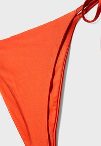 Bas de maillot de bain triangulaire orange vif avec liens latéraux réglables sur fond clair.