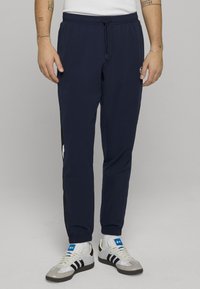 Donkerblauwe, lichtgewicht sportbroek met een elastische tailleband en trekkoord, voorzien van zwarte strepen aan de zijkant en een logo op het linker bovenbeen.