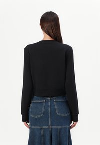 Sweatshirt preto curto com mangas longas, punhos canelados e gola redonda, combinado com uma saia de ganga azul com bolsos.