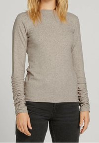 Långärmad topp i ljusbeige stickad tyg med rynkade detaljer vid handlederna. Har rund halsringning och en åtsittande silhuett.