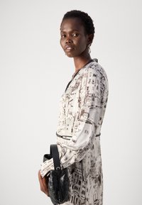 Long-sleeve dress featuring a monochrome cityscape print on a light background. Black belt accent and woven black handbag.