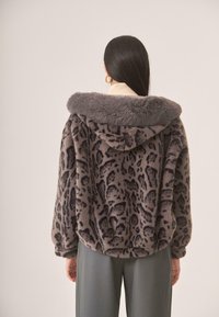 Sudadera de pelaje sintético en gris con estampado de leopardo negro, que cuenta con un suave y esponjoso cuello y un corte relajado. Combinada con pantalones gris claro.