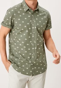 Chemise à manches courtes boutonnée en tissu vert olive, avec un motif de palmiers blancs, col et poignets retroussés. Texture lisse, design décontracté.