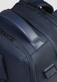 Marineblauwe rugzak met gestructureerde stof, dubbele ritsen, een gevoerd handvat en een subtiele logokleur aan de voorkant.