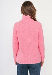 Pull en tricot rose côtelé avec col montant et manches raglan ; texture douce et coupe décontractée, dos du porteur faisant face à la caméra.
