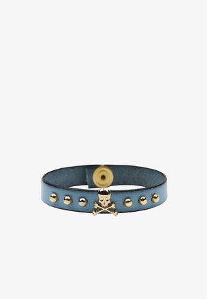 Bracciale in pelle blu con dettaglio di teschio e ossa incrociate in tonalità dorata. Presenta borchie metalliche e chiusura a scatto. Forma arrotondata, texture liscia.