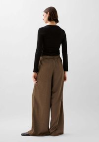 Zwarte lange mouw top met geribbelde textuur, gecombineerd met loszittende bruine broek met elastische tailleband en subtiel patroon.